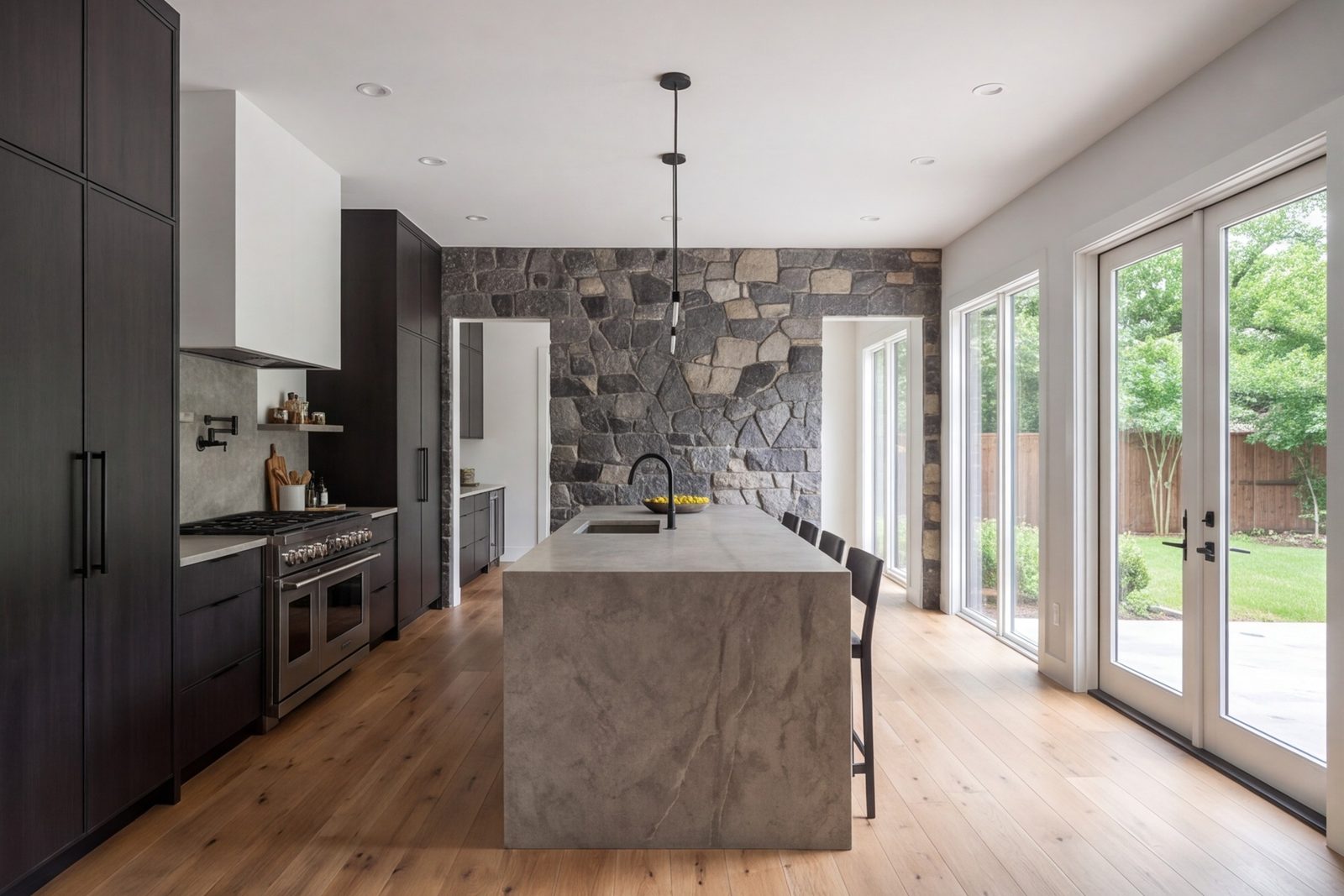 Modern kitchen with a long island, full-height cabinets and a stone range wall, seen from the dining area